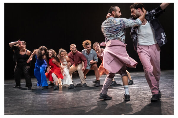 Een kleurrijke groep dansers in diverse outfits voert energiek op, sommigen in beweging, anderen in dynamische, expressieve houdingen.

A colorful group of dancers in varied outfits perform energetically on stage, some in motion, others in dynamic, expressive poses.