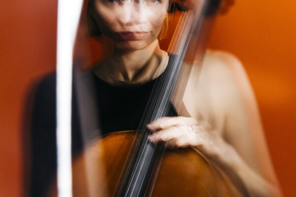 Woman plays a cello in an orange-lit room, with motion blur creating a dynamic atmosphere.