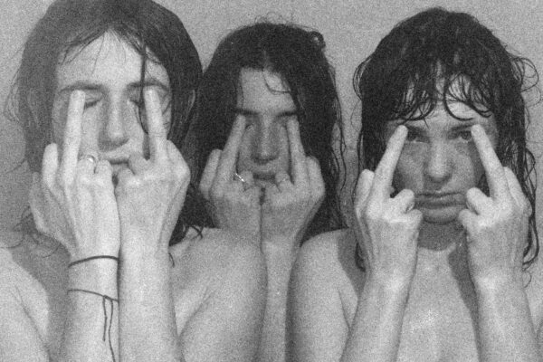 Three people cover their faces by holding their raised middle fingers before their faces in a black-and-white, grainy image.