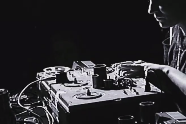 Silhouette of a person at a lit DJ setup with turntables and mixers in the dark."