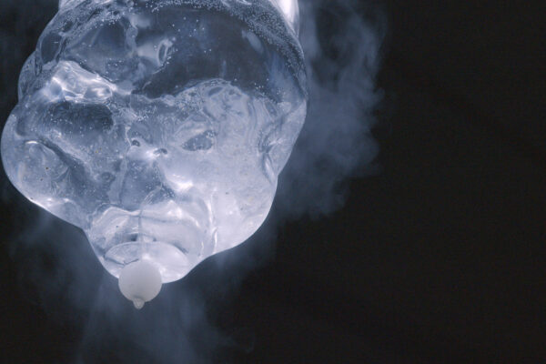Close-up of a wet glass sculpture with droplets and a white cap against a dark background.