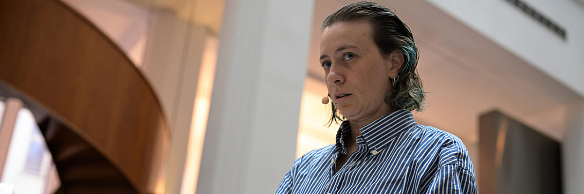 Person in striped shirt holds aluminium foil in their hands, standing in a large space with white columns.